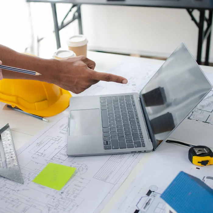 Ingegnere consulta planimetrie con computer in cantiere